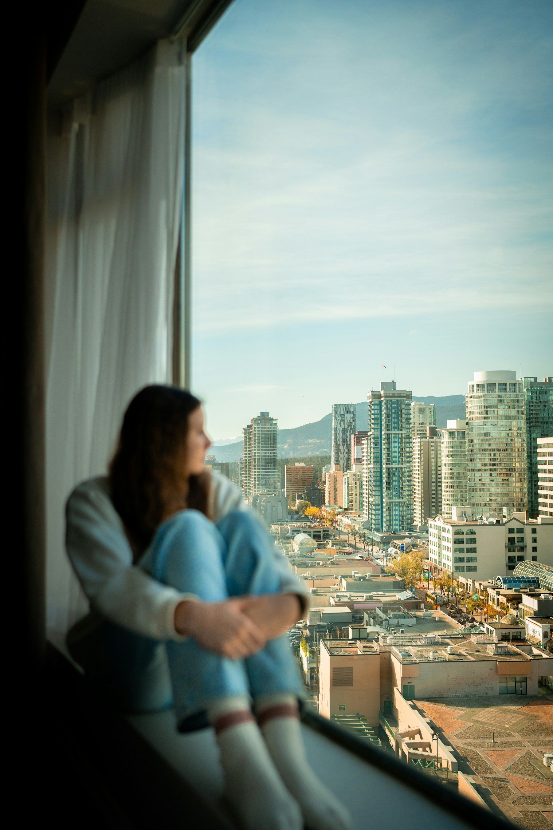 Mujer sentada junto a la ventana de su casa, mirando la ciudad en la que vive.